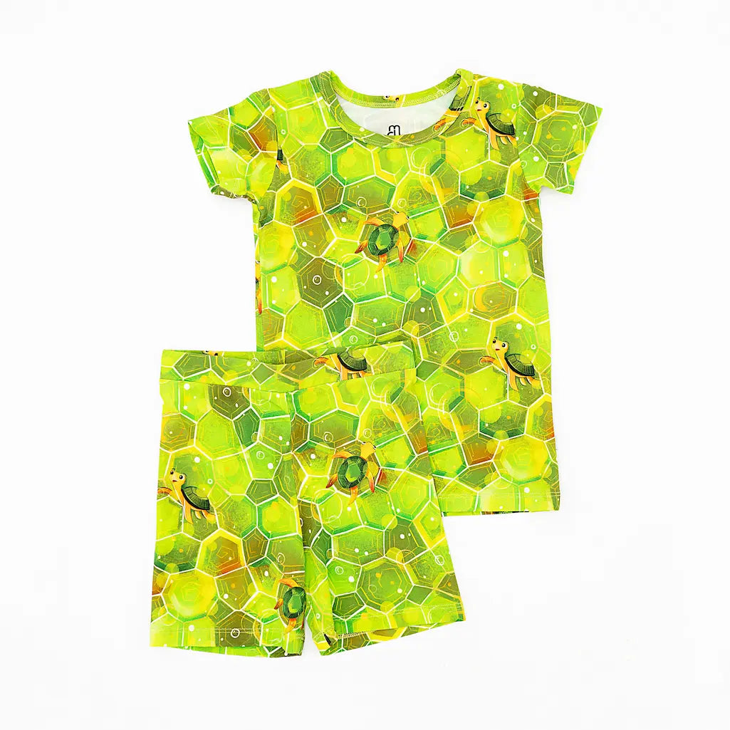 A short pajama set for children with a geometric green shell pattern and hexagonal design, resembling a sea turtle's back.