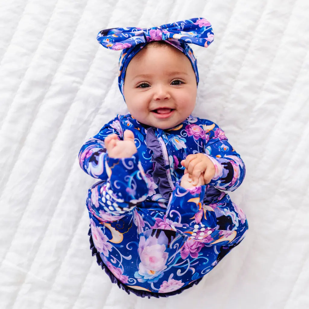 Baby wearing a colorful outfit with a matching headband on a white blanket