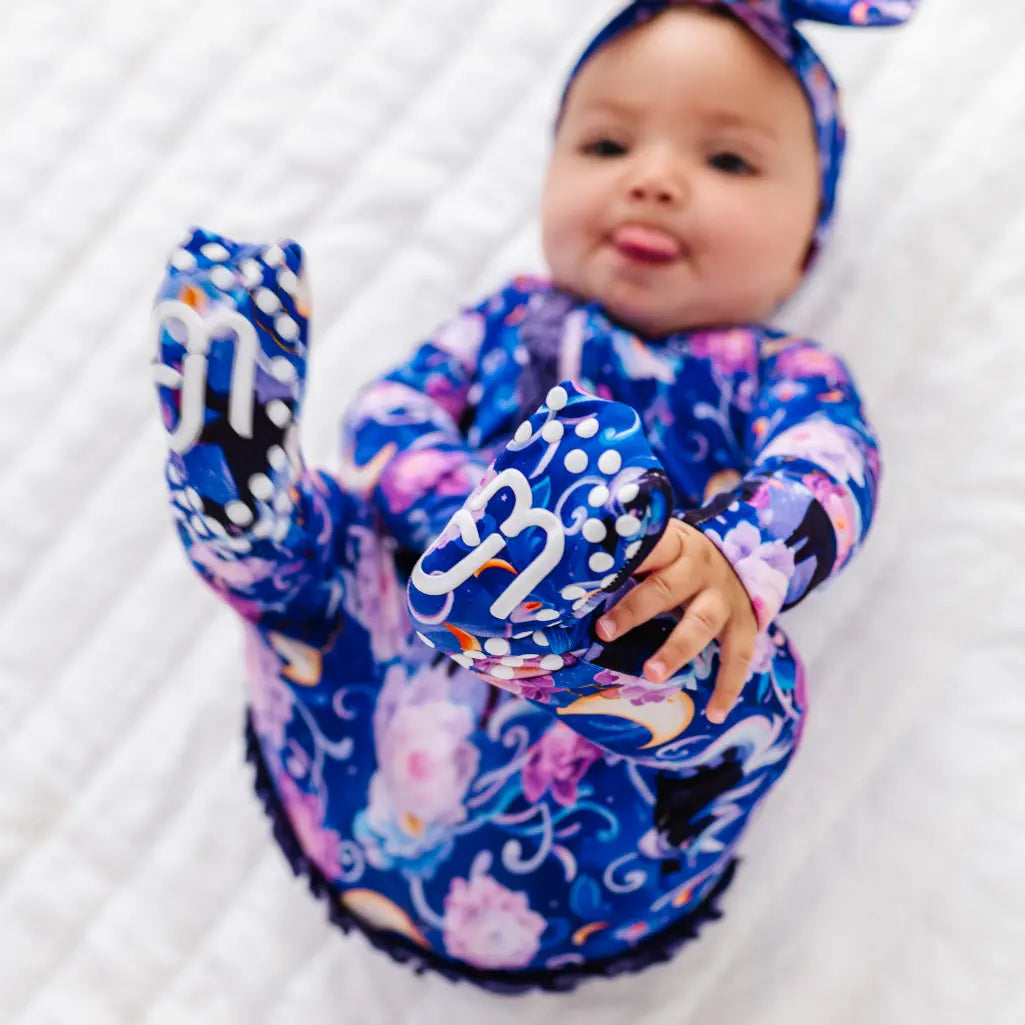Child wearing a colorful floral swimsuit sitting on a white floor with greenery in the background
