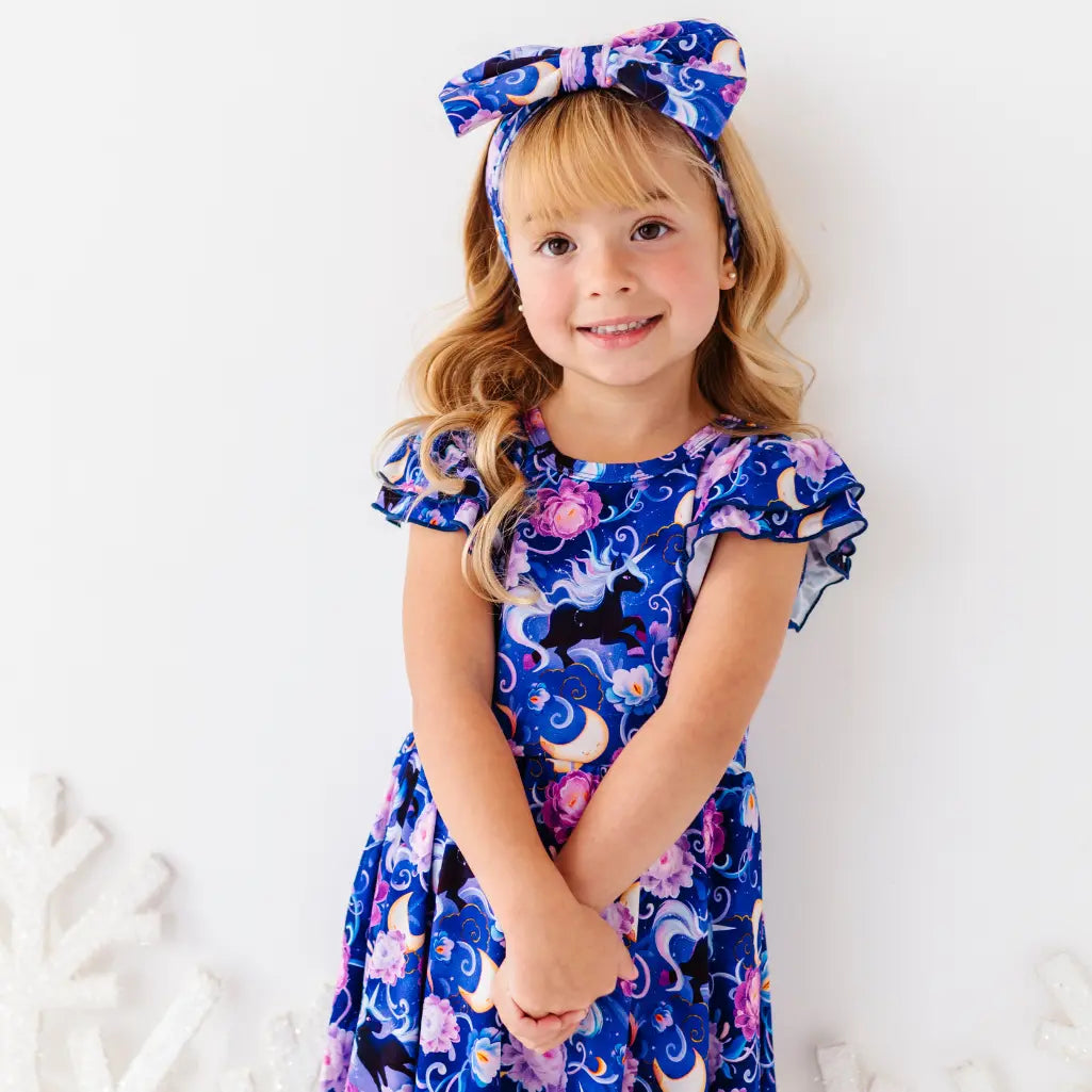 Young girl wearing a blue dress with a floral and animal pattern, standing against a white background.