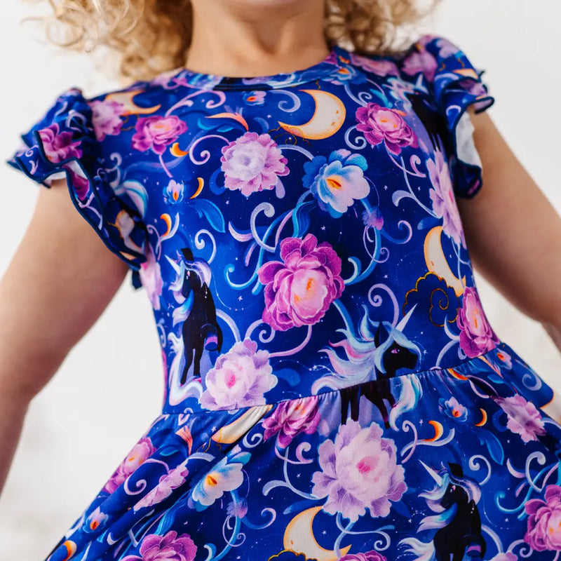 Child wearing a blue dress with floral and unicorn designs on a white background