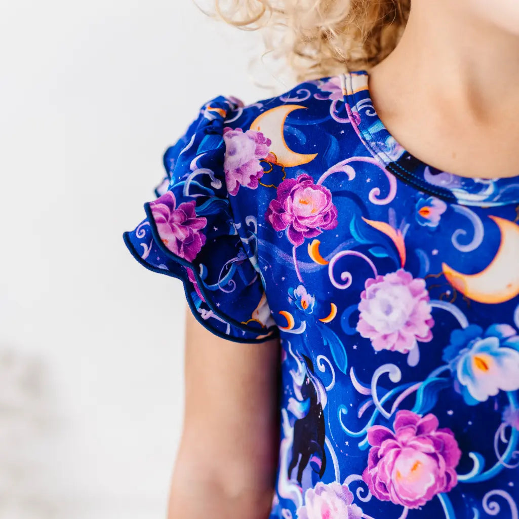 Child wearing a blue dress with floral and moon designs on a white background