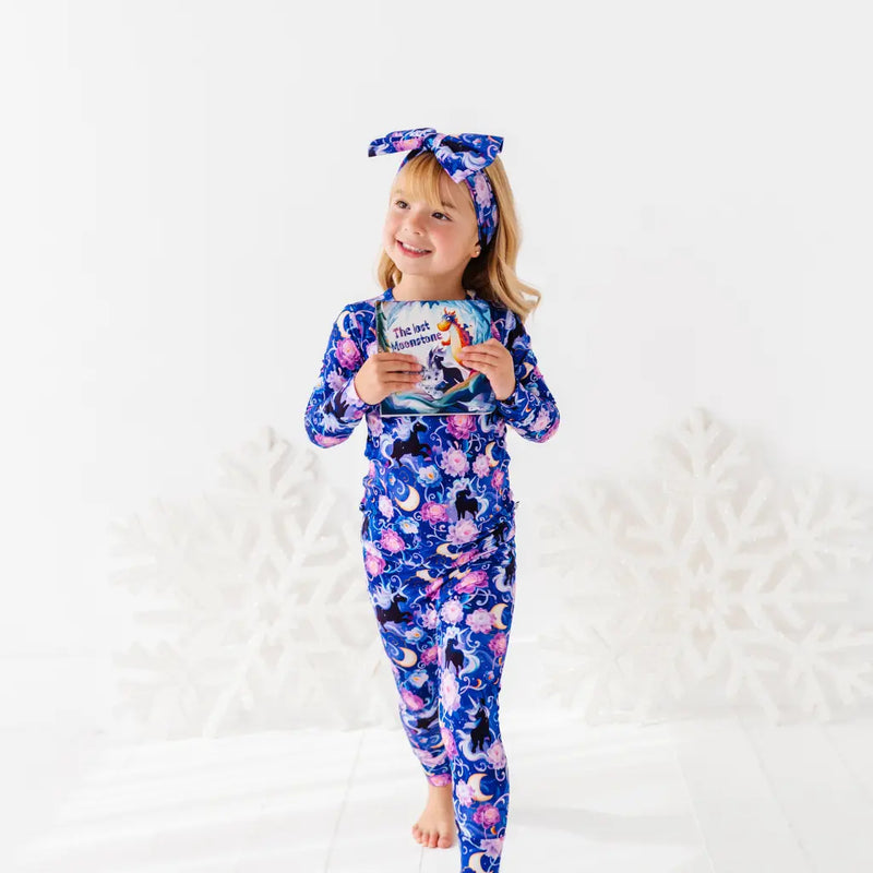 Child wearing a blue and pink outfit with a matching headband, holding a book on a white background.