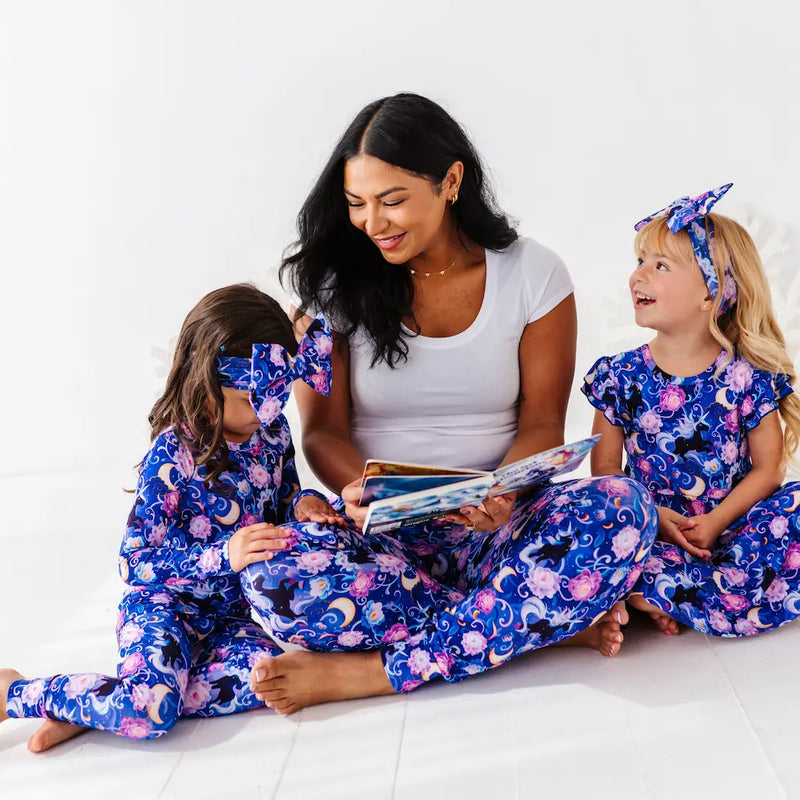 Woman and two children in matching pajamas reading a book on a white background