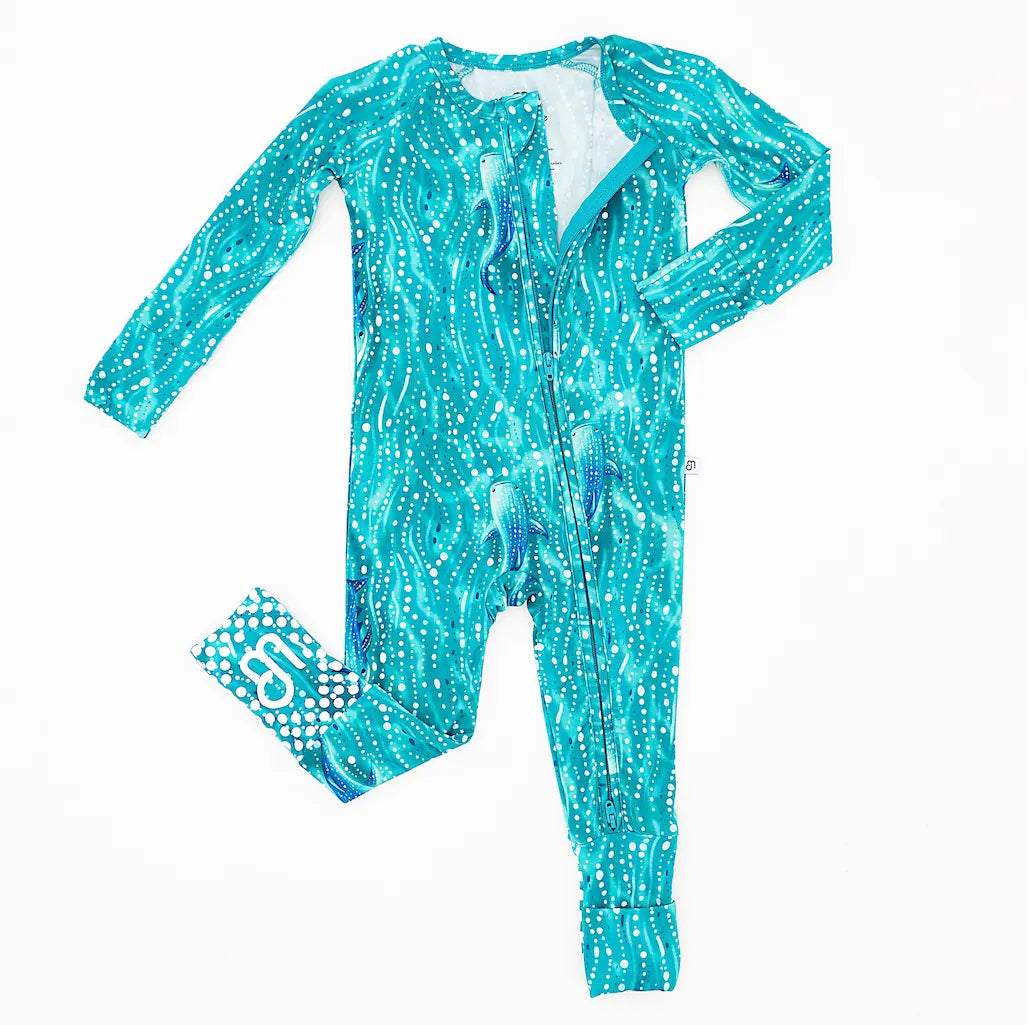 A onepiece zipper pajama for babies with a print inspired by whale sharks and teal waves, including convertible foot covers and fold-over mittens.
