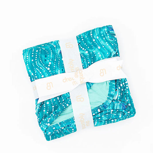 A folded blanket with a geometric pattern featuring teal colors and white details, wrapped with a ribbon.