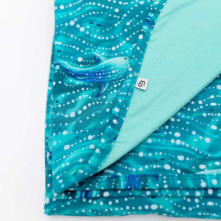 A folded blanket with a vibrant teal color and a pattern featuring a whale shark swimming in the ocean.