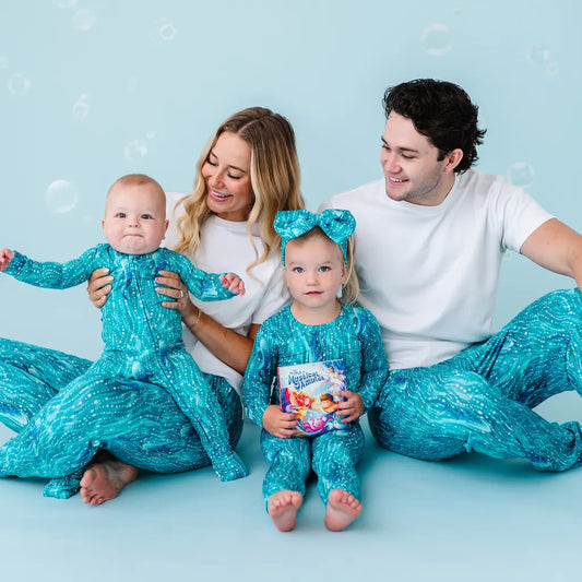 Family of four in matching teal outfits on a light blue background.
