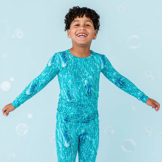 A child wearing a long sleeve top and matching pants with a blue and white whale shark and wave pattern.