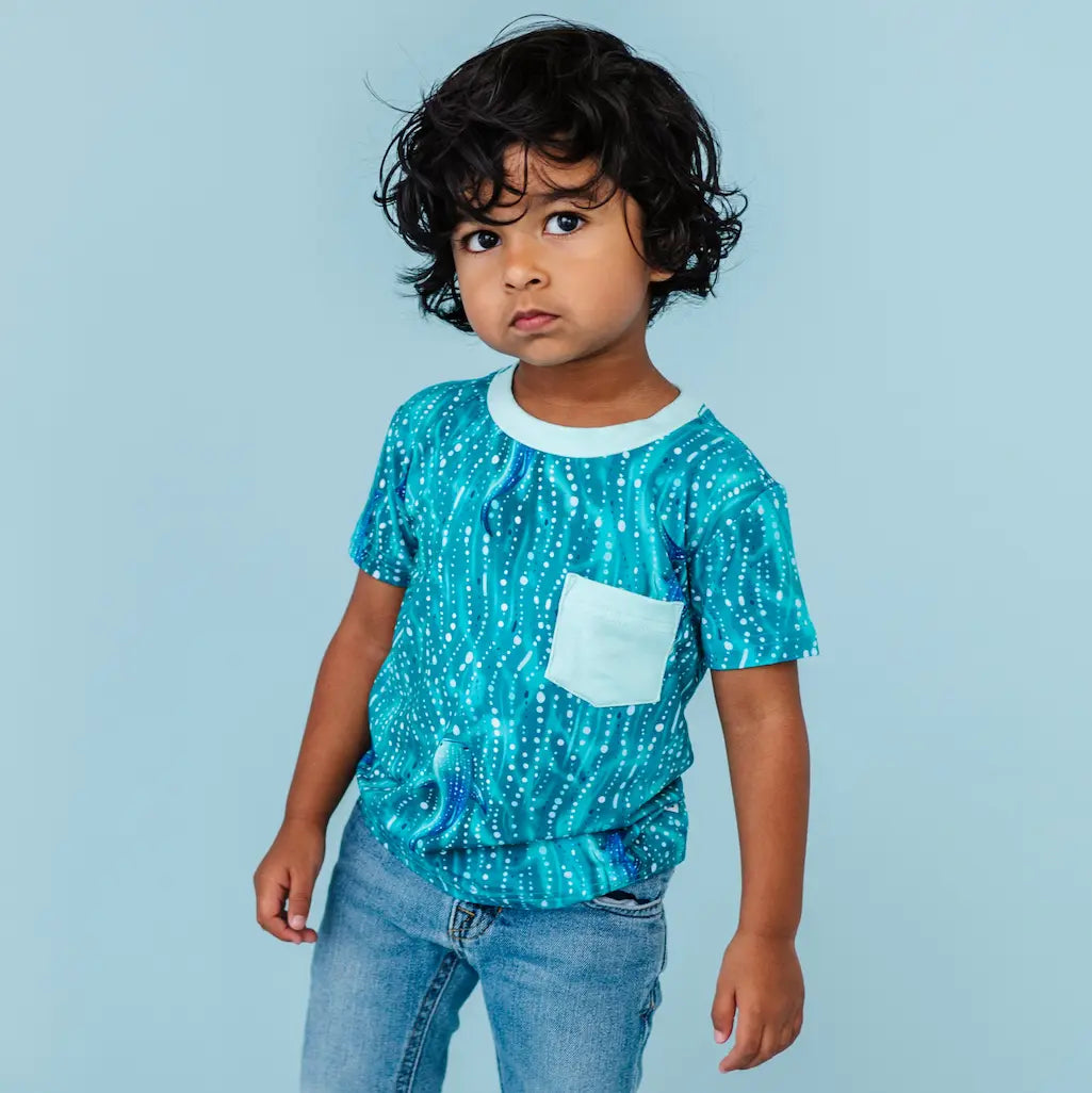 Child wearing a blue patterned shirt with a pocket on a light blue background