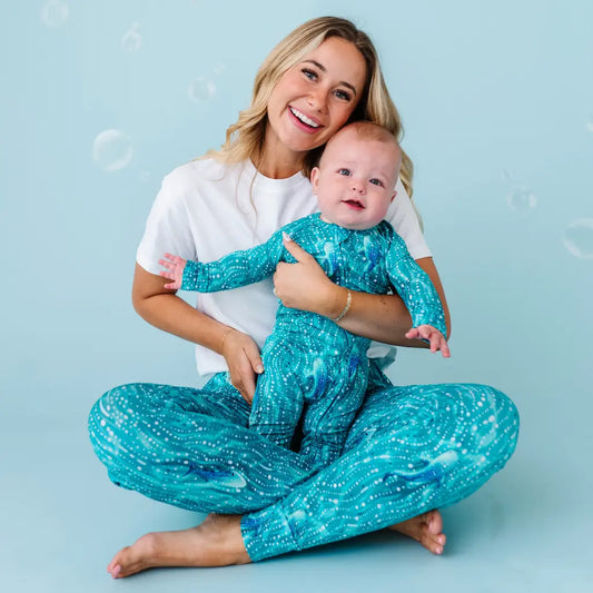 Woman and baby sitting on a blue background wearing matching teal outfits.