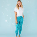 A woman standing and smiling, wearing white shirt and blue pajama pants with a whale shark and underwater design.