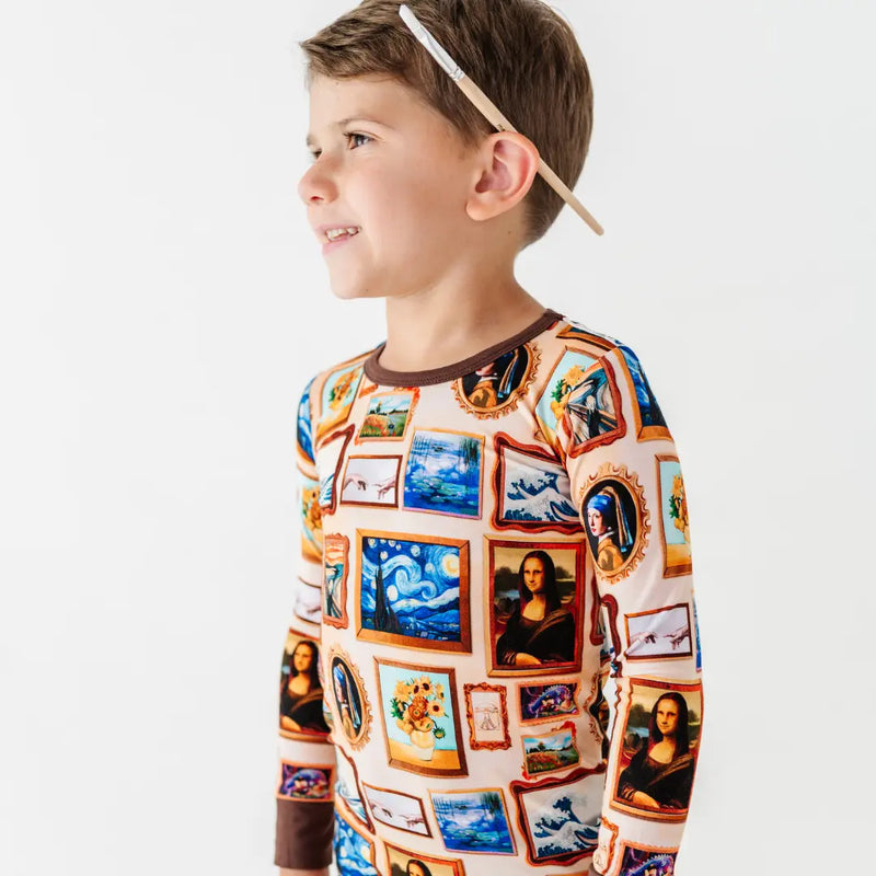 A smiling child with a paintbrush behind one ear, wearing a pajama top printed with framed classic paintings.