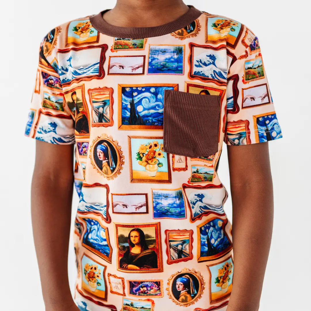 Close-up of a short-sleeve pocket tee printed with framed classic paintings, with a brown ribbed collar and chest pocket.