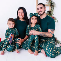 A family of four sitting close together and smiling at the camera in matching pajamas in a dark green print of gold Christmas trees and dark green tees.