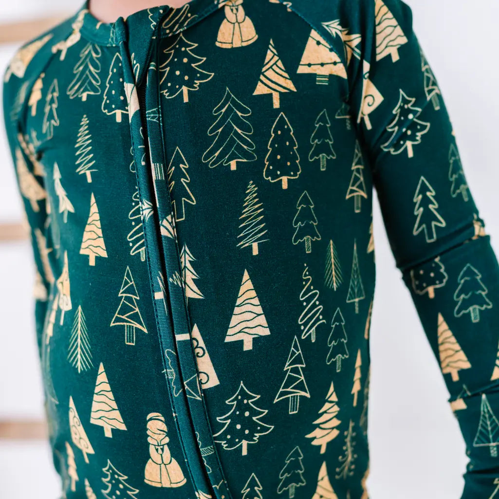 Close up of the front zipper and chest of a zip up baby pajama in a dark green print of gold Christmas trees.