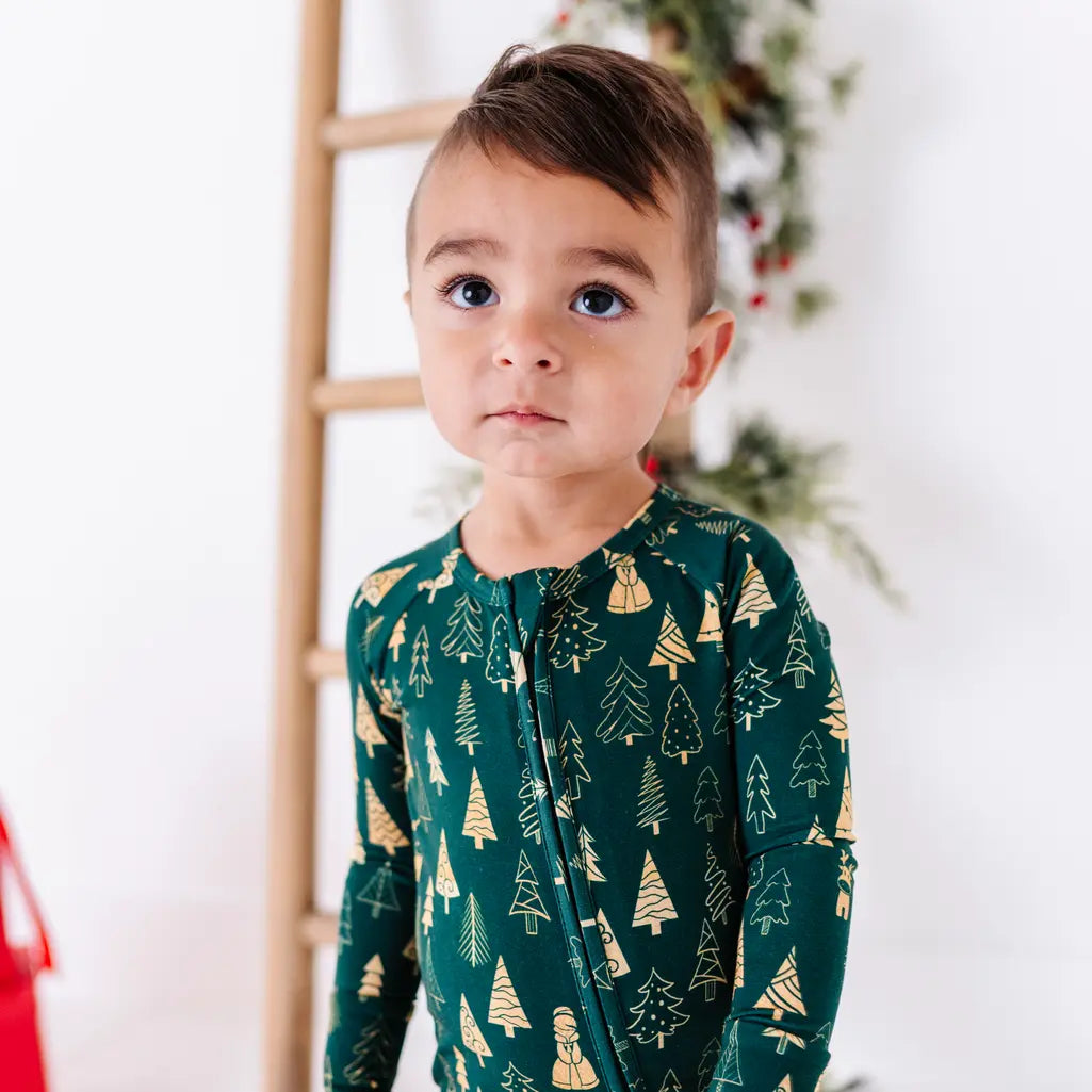 Close up portrait of a toddler looking up, wearing a zip up pajama in a dark green print of gold Christmas trees.