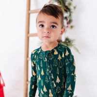 Close up portrait of a toddler looking up, wearing a zip up pajama in a dark green print of gold Christmas trees.