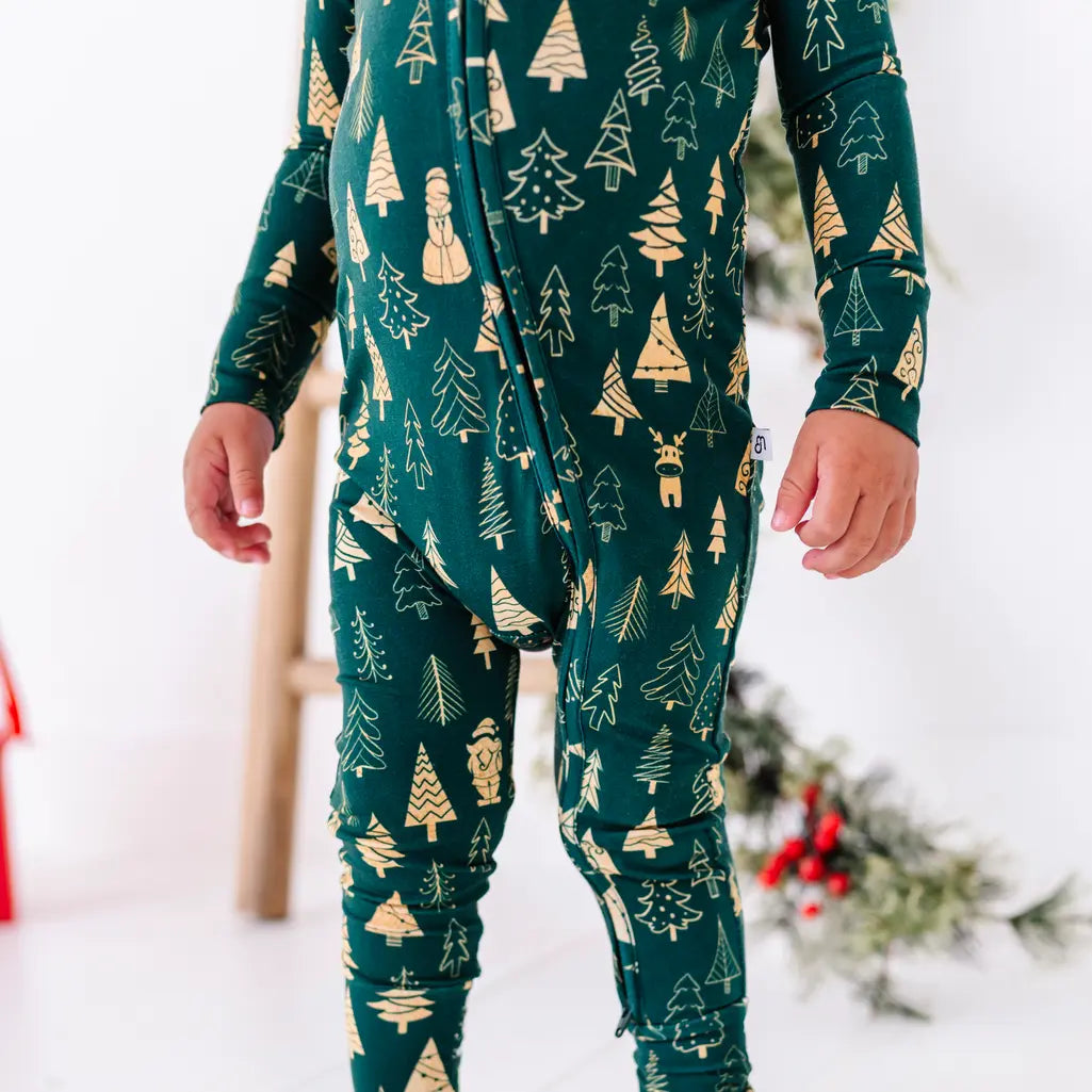 Close up of the zipper front and legs of a zip up pajama on a standing toddler, in a dark green print of gold Christmas trees.
