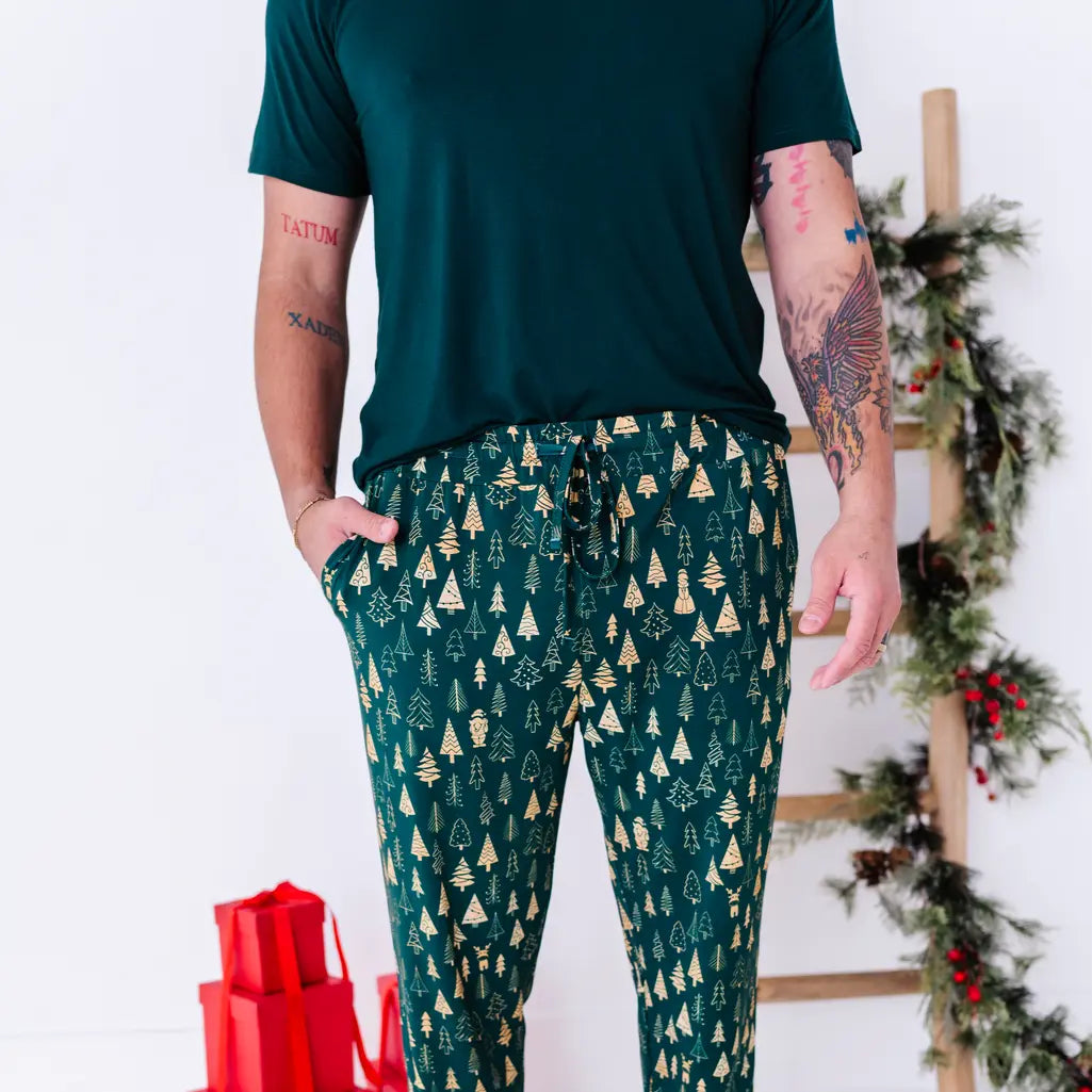 Close up of the drawstring waist and side pocket of jogger pajama pants in a dark green print of gold Christmas trees, with a dark green tee.