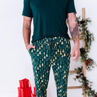 Close up of the drawstring waist and side pocket of jogger pajama pants in a dark green print of gold Christmas trees, with a dark green tee.