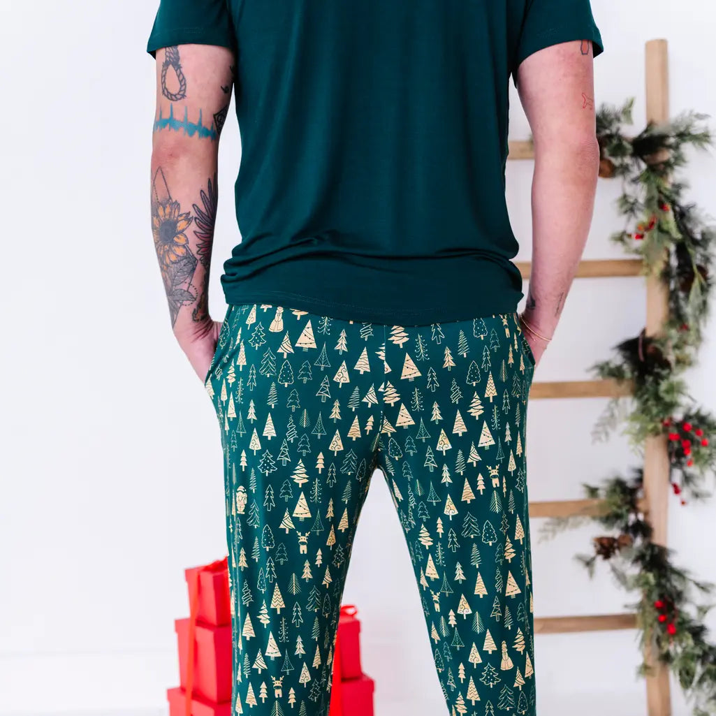Back view of a man in a dark green tee and jogger pajama pants in a dark green print of gold Christmas trees.