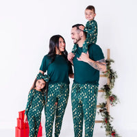 Two adults laughing together, one carrying a child on the shoulders, in matching pajamas in a dark green print of gold Christmas trees and dark green tees.