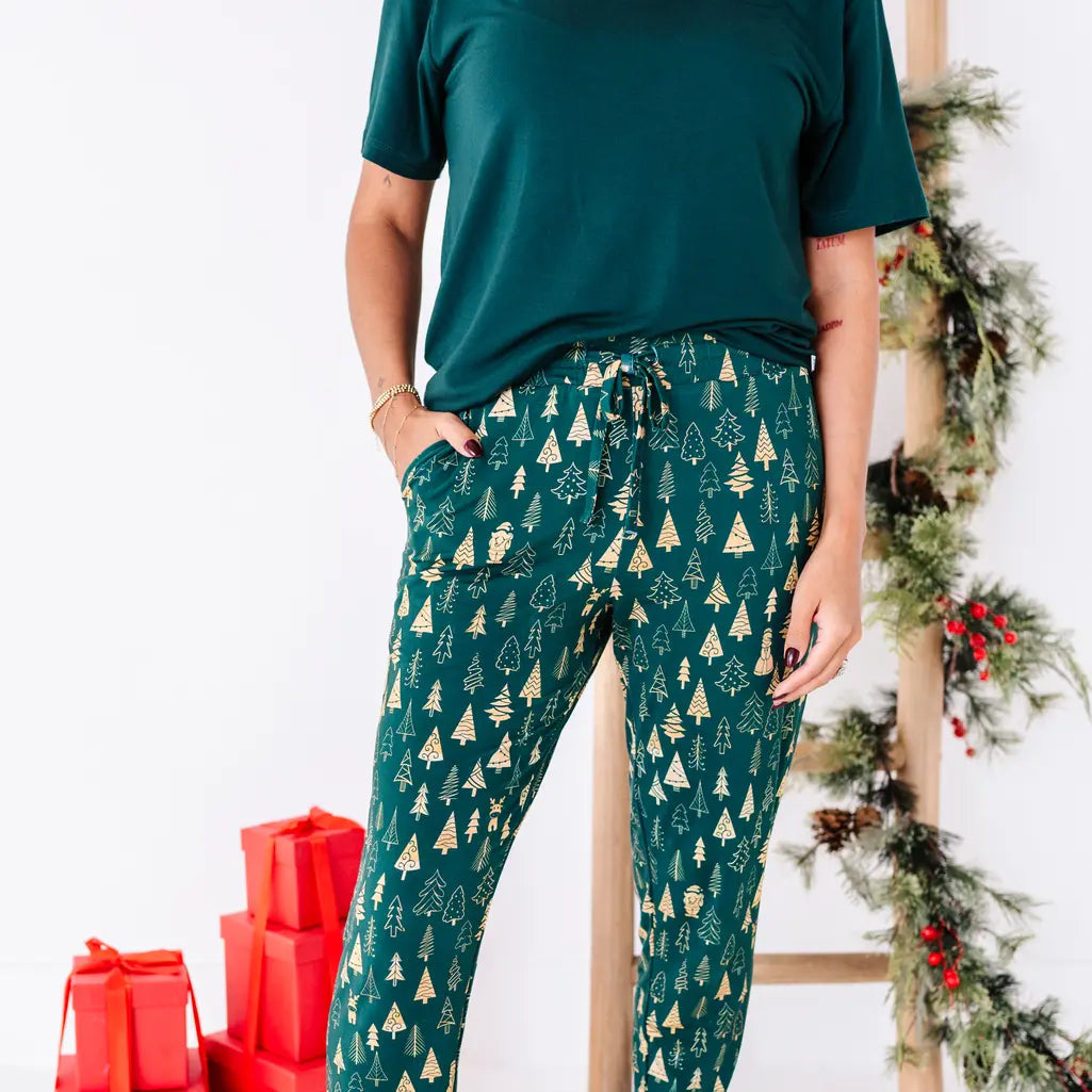 Close up of the waist and legs of jogger pajama pants with a drawstring and pocket in a dark green print of gold Christmas trees.