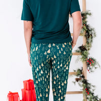 Back view of jogger pajama pants in a dark green print of gold Christmas trees, with a dark green tee.