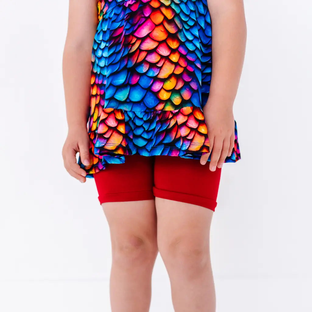 Close up of the ruffled hem of a flutter sleeve peplum top in a rainbow dragon scale print over red bike shorts.