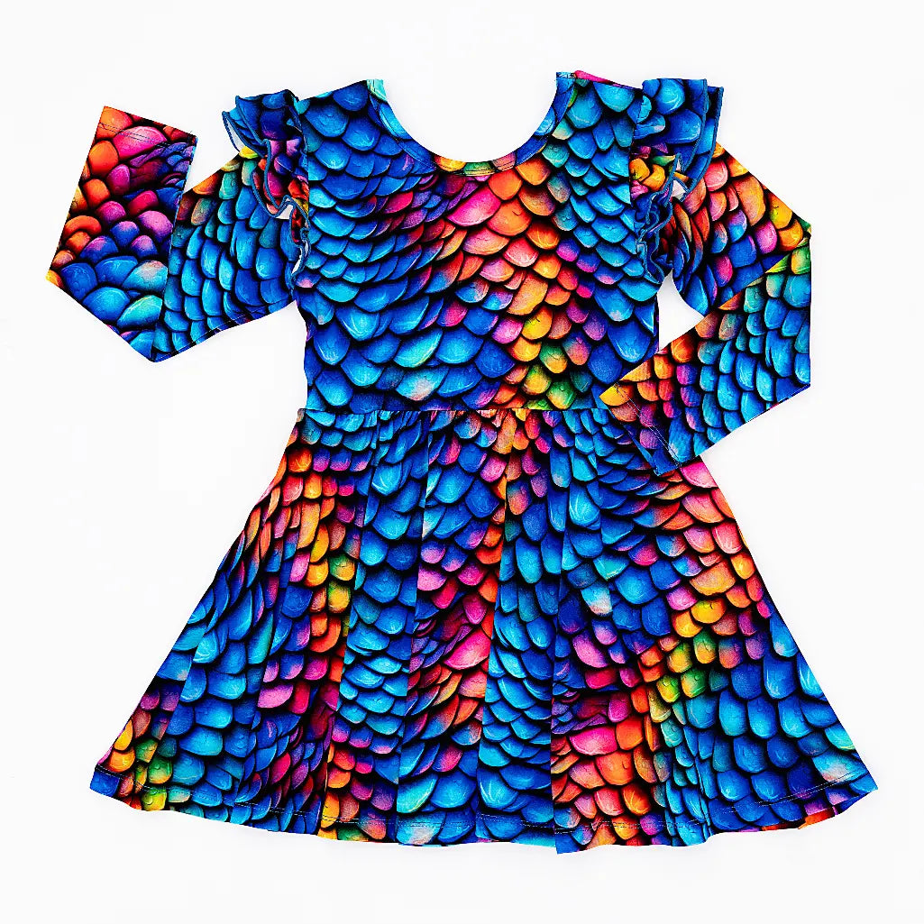 Flat lay of a long sleeve twirl dress with flutter ruffles at the shoulders in a rainbow dragon scale print of blue, pink, orange, and yellow on a white background.