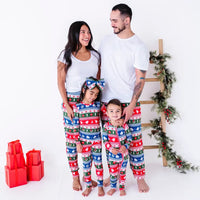 Two adults laughing together while two kids smile at the camera, all in matching pajamas in red, green, blue, and white fair isle stripes with snowflakes, pine trees, and white dragon heads.