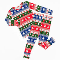 Flat lay of a long sleeve pajama top and matching pants in red, green, blue, and white fair isle stripes with snowflakes, pine trees, and white dragon heads on a white background.