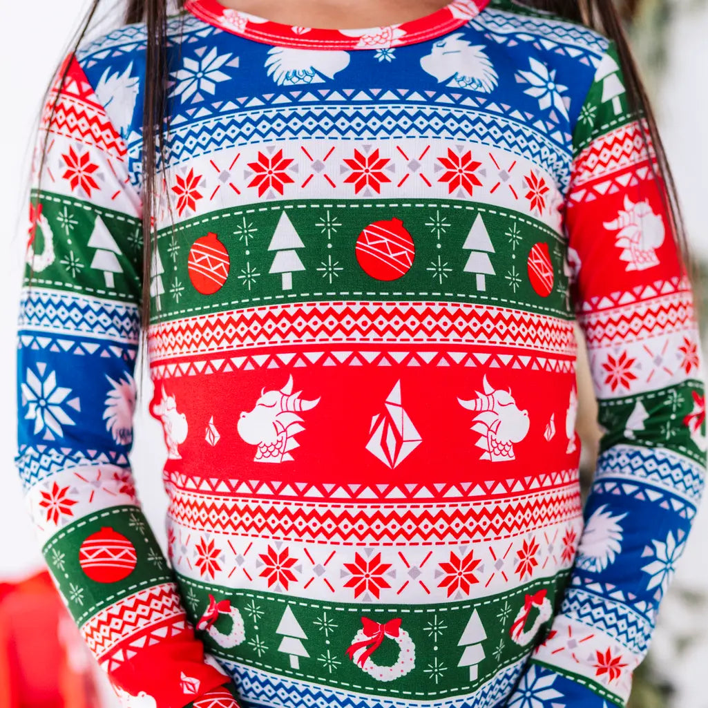 Close up of the chest and sleeves of a long sleeve pajama top in red, green, blue, and white fair isle stripes with snowflakes, pine trees, and white dragon heads.