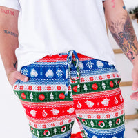 Close up of the drawstring waistband and pocket of jogger pajama pants in red, green, blue, and white fair isle stripes with snowflakes, pine trees, and white dragon heads.