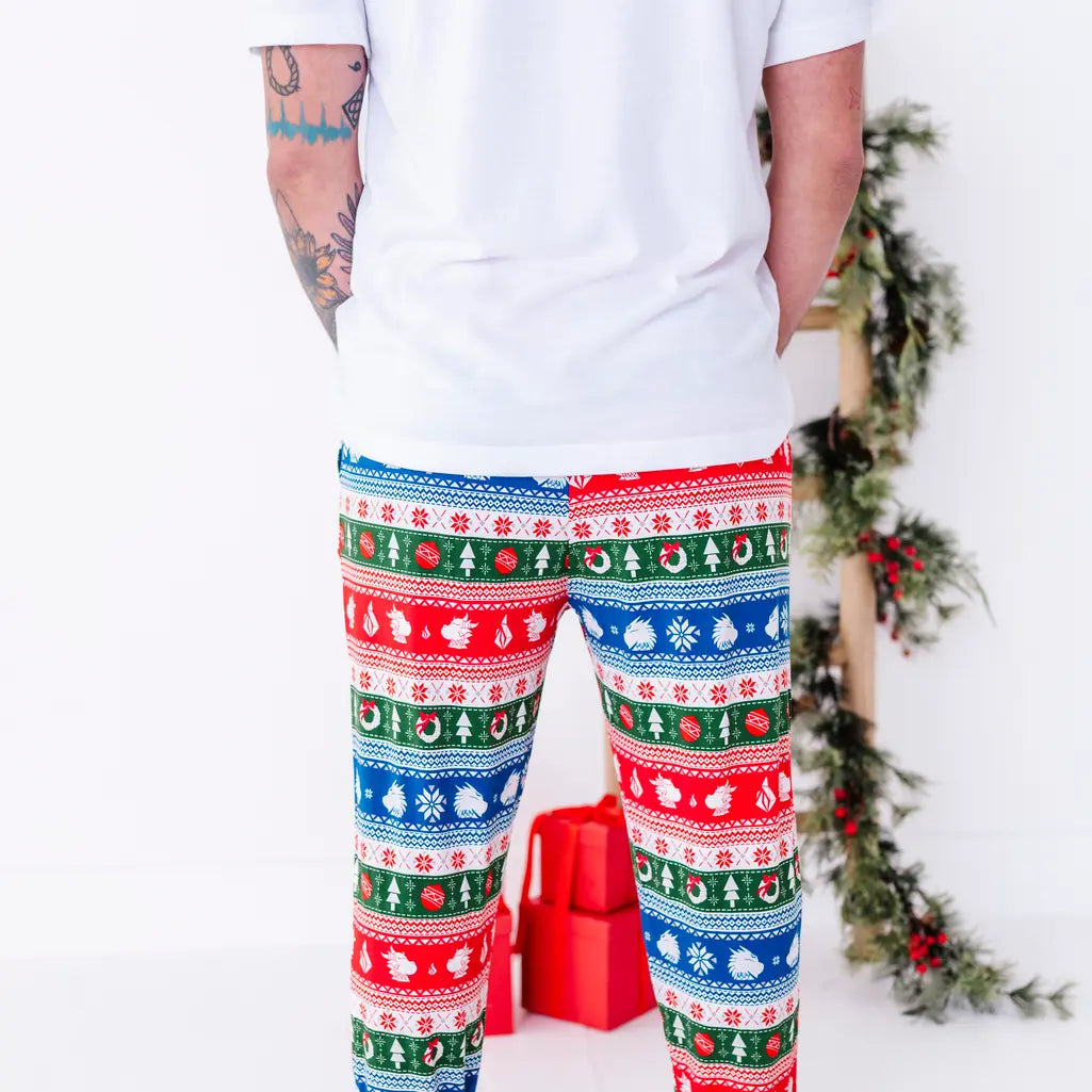 Back view of a man standing in a white tee and jogger pajama pants in red, green, blue, and white fair isle stripes with snowflakes, pine trees, and white dragon heads.