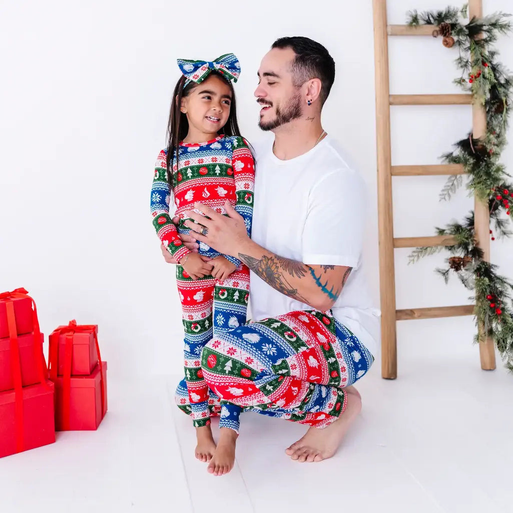 An adult laughing while holding a child close, in matching pajama pants and a pajama set in red, green, blue, and white fair isle stripes with snowflakes, pine trees, and white dragon heads.