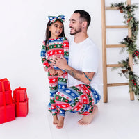 An adult laughing while holding a child close, in matching pajama pants and a pajama set in red, green, blue, and white fair isle stripes with snowflakes, pine trees, and white dragon heads.