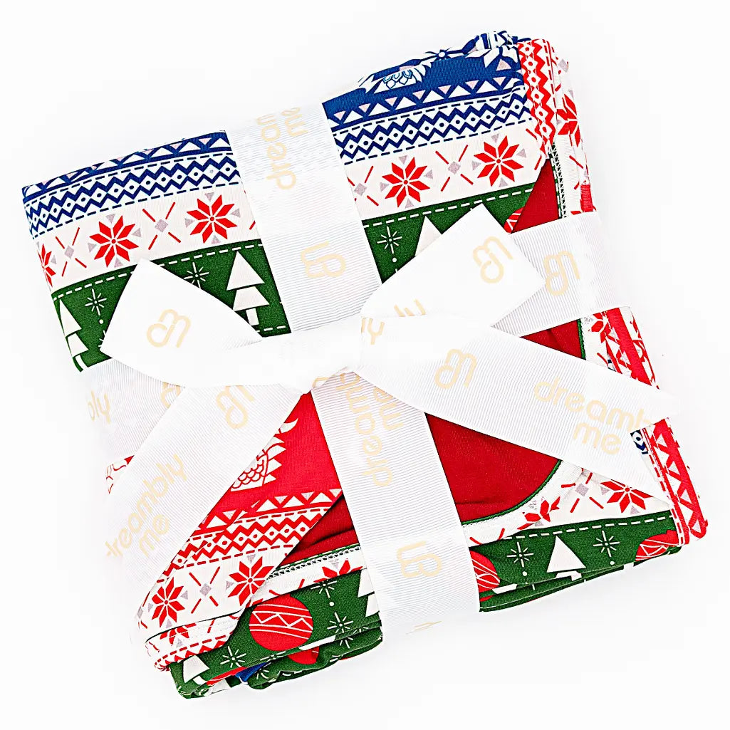 Flat lay of a folded blanket tied with a white ribbon in a red, green, blue, and white fair isle print with snowflakes and pine trees on a white background.