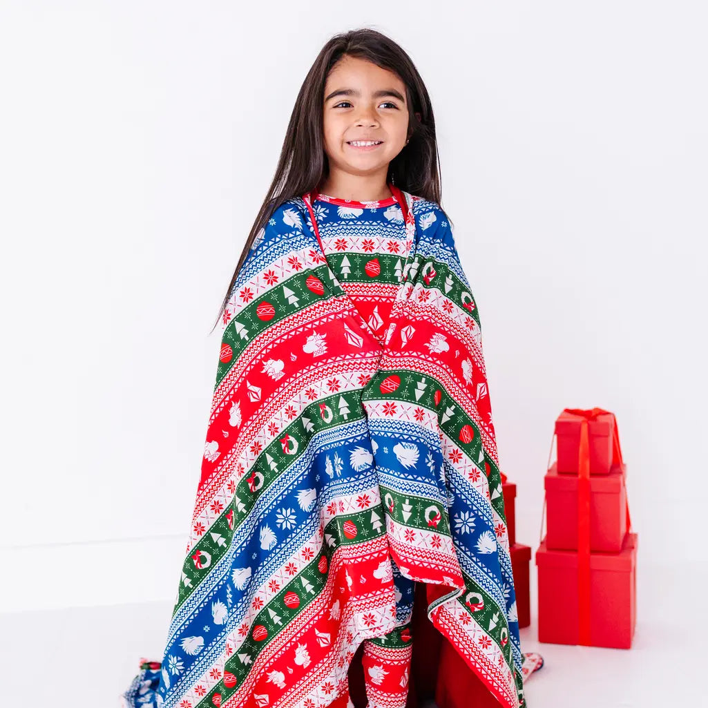 A child with a big smile wrapped in a blanket in a red, green, blue, and white fair isle print with snowflakes and pine trees.