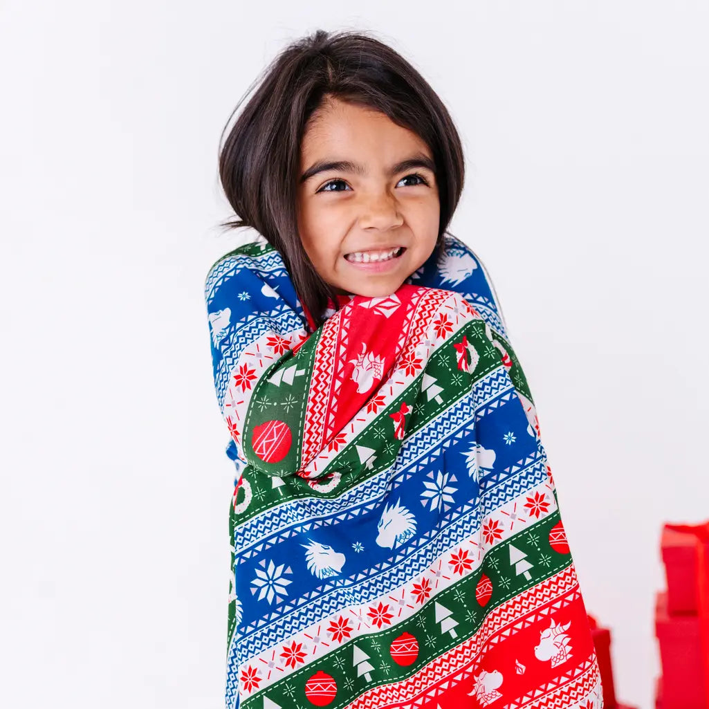 Close up of a child with a big smile wrapped in a blanket in a red, green, blue, and white fair isle print with snowflakes and pine trees.