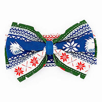 Flat lay of a large fabric bow headband in a red, green, blue, and white fair isle print with snowflakes and white dragon heads on a white background.
