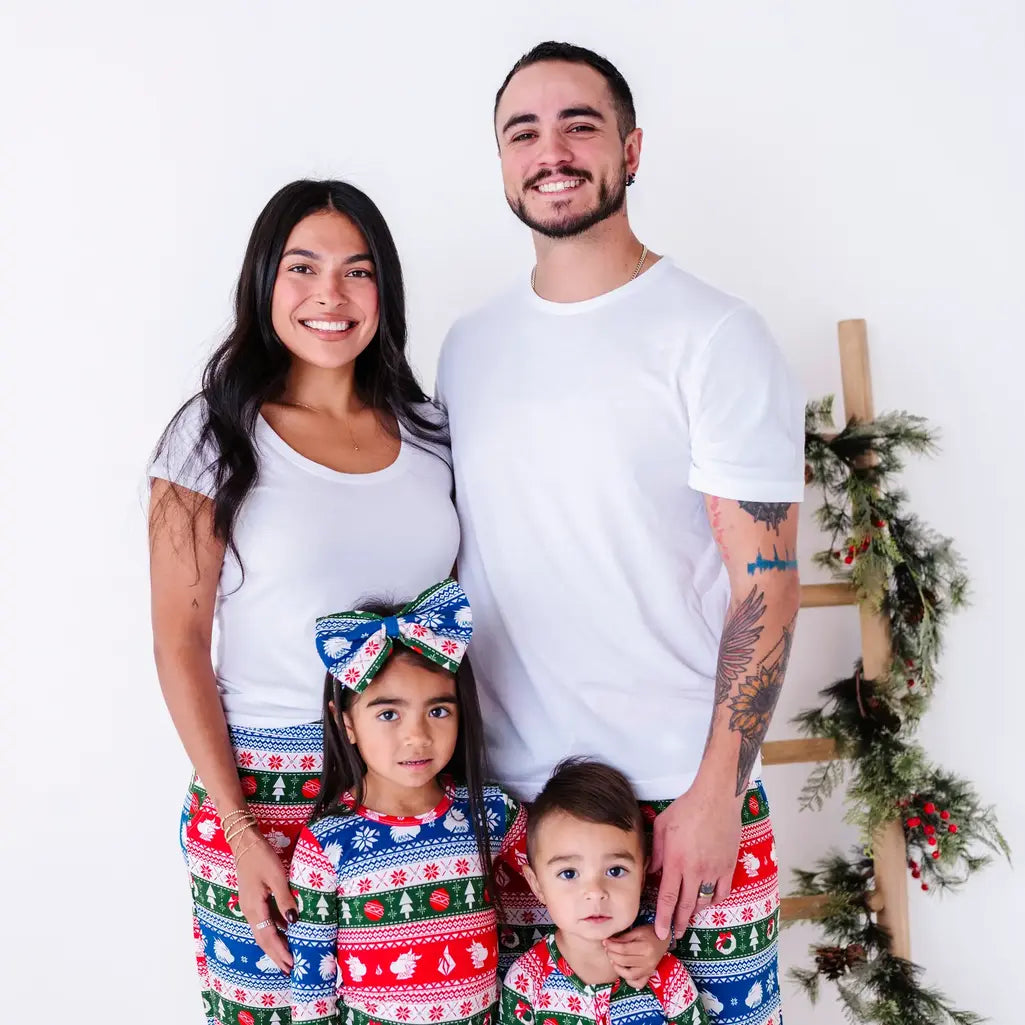 A close family portrait of two adults and two kids, all smiling in matching pajamas in red, green, blue, and white fair isle stripes with snowflakes, pine trees, and white dragon heads.