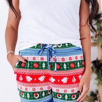 Close up of the drawstring waistband and pocket of jogger pajama pants in red, green, blue, and white fair isle stripes with snowflakes, pine trees, and white dragon heads.