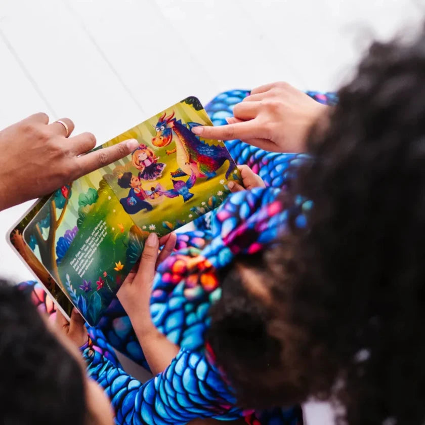 Two children in blue dragon scale pajamas pointing at a page of an open storybook, seen from above.