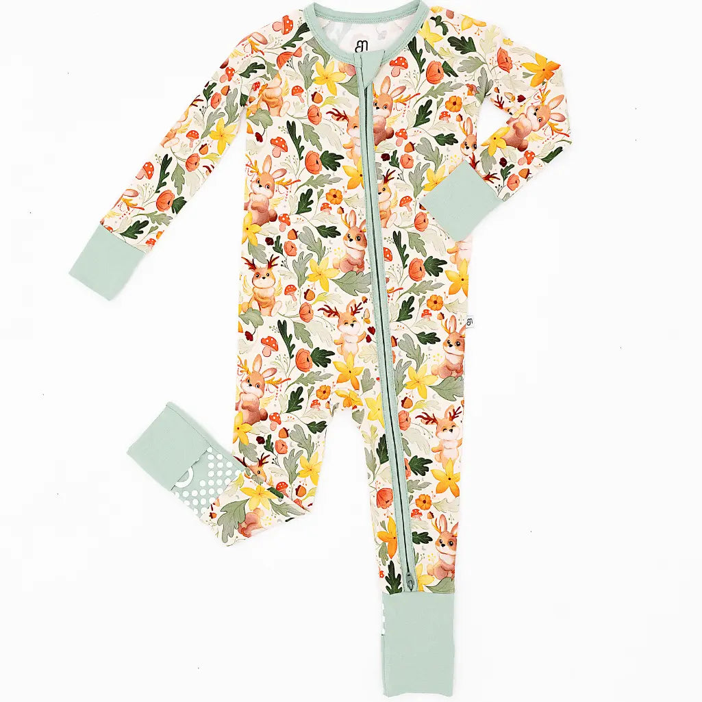 A zip up baby pajama with sage green fold over cuffs laid flat on a white background in a woodland jackalope print.