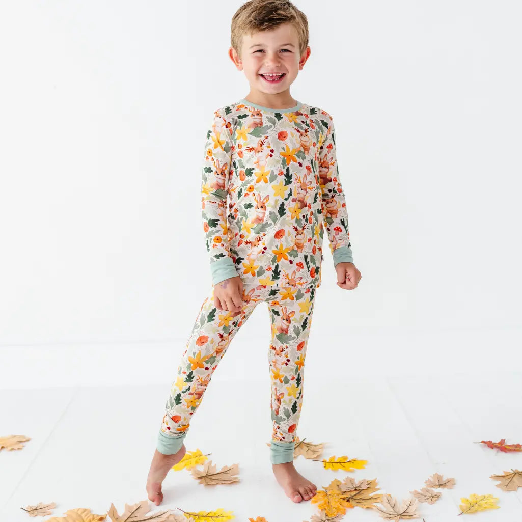 A child standing barefoot on a white floor with leaves wearing a woodland print two piece pajama set.