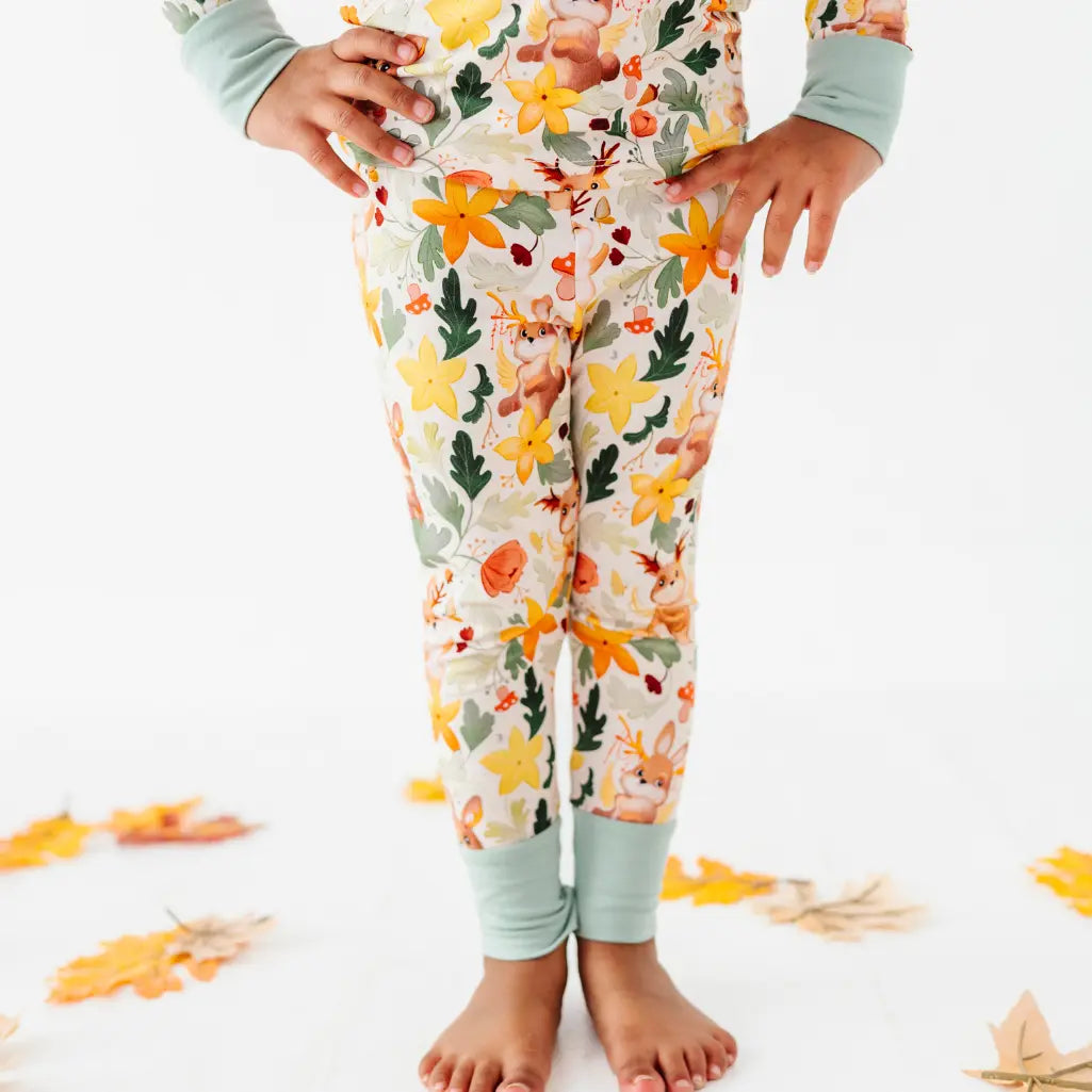 A cropped view of a child's legs in woodland print pajama pants with sage green ankle cuffs.