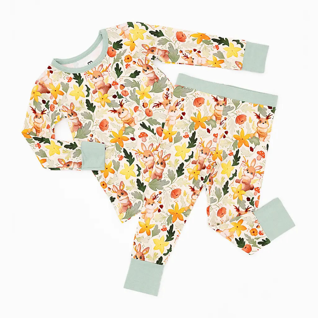 A long sleeve pajama top and matching pants with sage green cuffs laid flat on a white background in a woodland jackalope print.