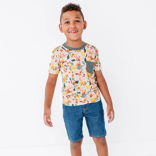 A child standing on a white background wearing a woodland jackalope print pocket tee with denim shorts.